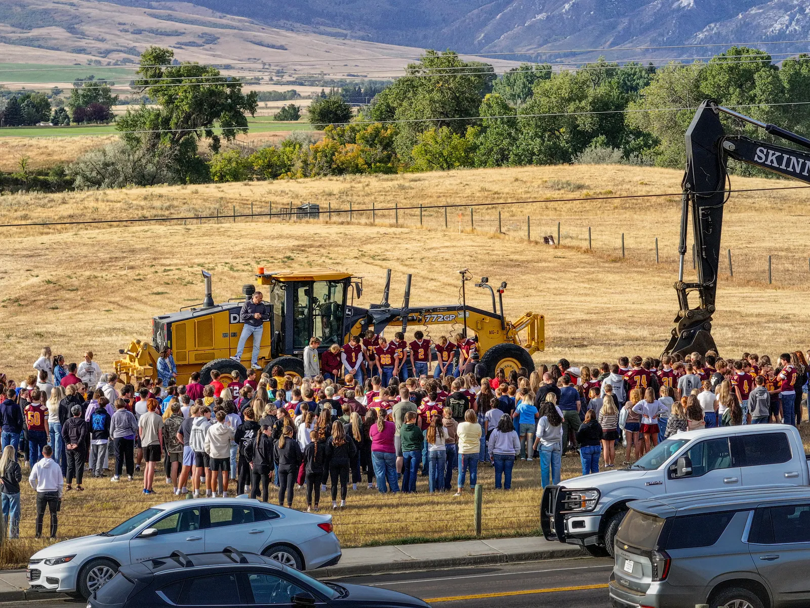 A crowd of students and community members surrounds the groundbreaking ceremony beside construction equipment.