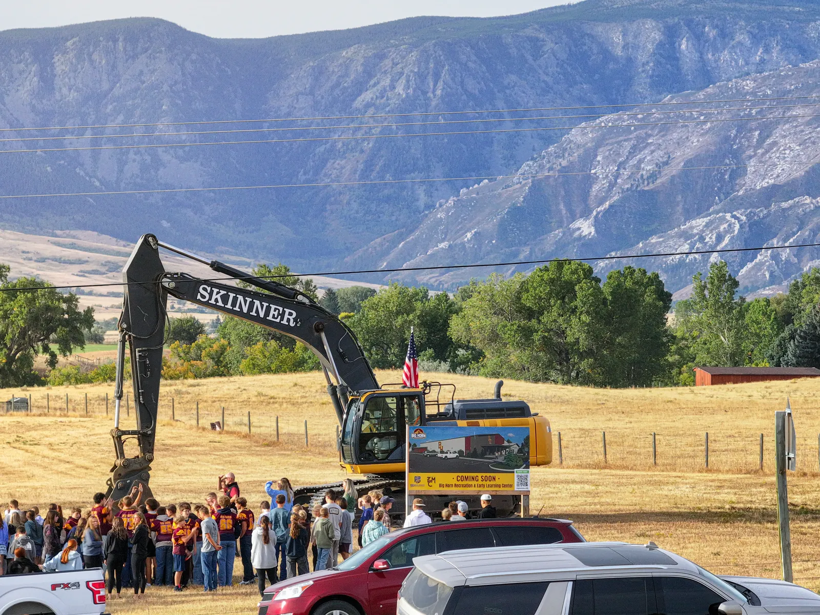 An excavator and the recreation center coming soon sign at the site, with the mountains behind them.